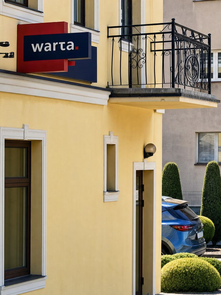 Wejście do biura przy ul. Traugutta 7B w Człuchowie — żółty budynek z czerwonym szyldem Warty nad wejściem